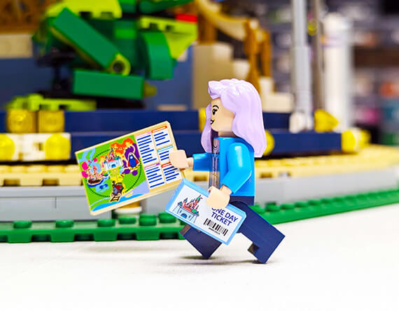 Minifig holding a printed theme pok ticket and map with a blurred LEGO set in the background. Custom printed theme park items.
